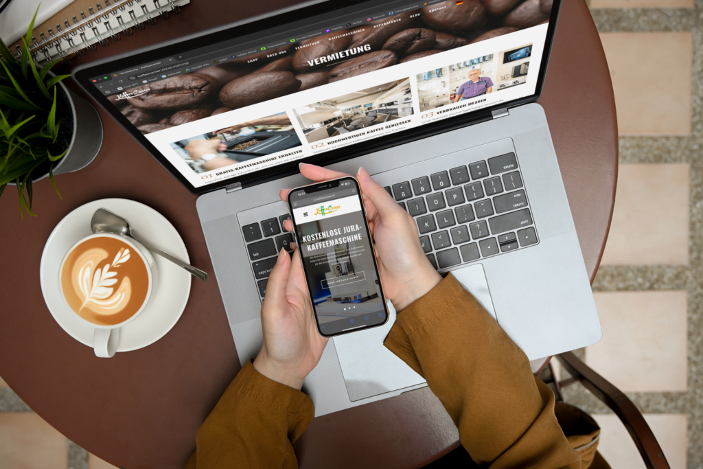 A top-down view of a MacBook and an iPhone displaying the Kaffeecenter GmbH online shop, with a cup featuring latte art next to them