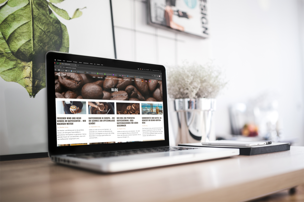 A MacBook on a desk, displaying the blog overview for Kaffeecenter GmbH and four posts