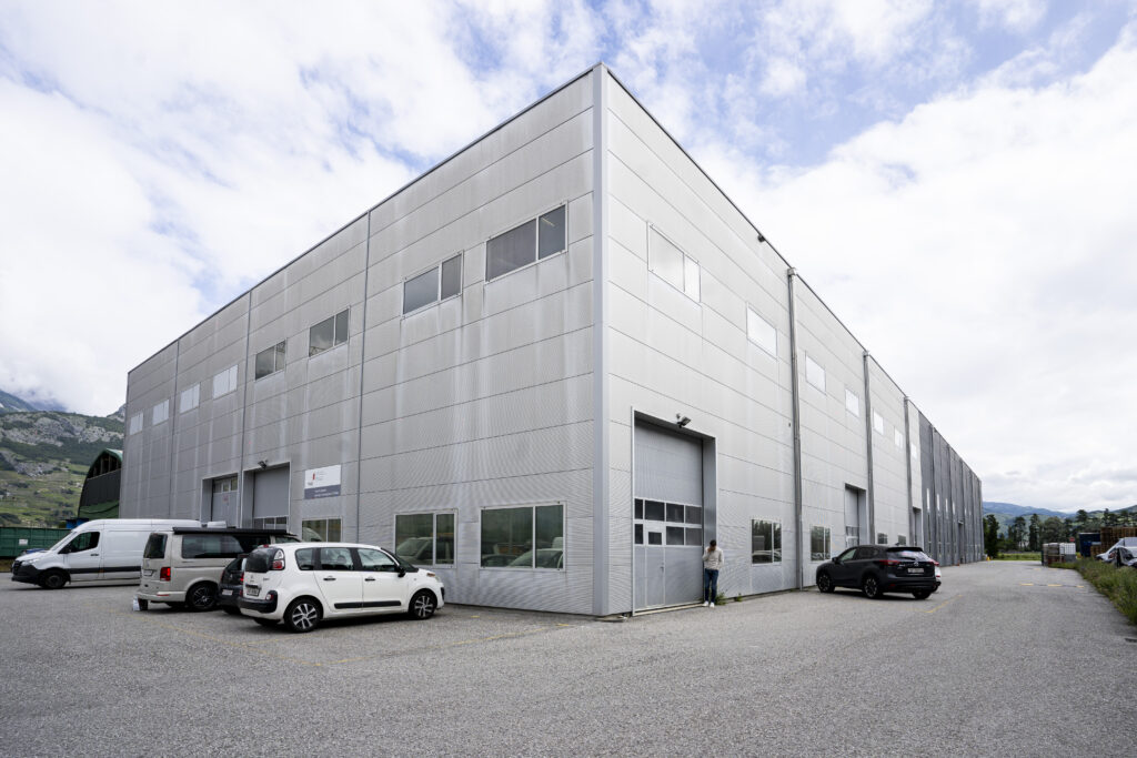 The second, light-grey warehouse on the Westgate site in Vétroz, with roller shutters and delivery vans
