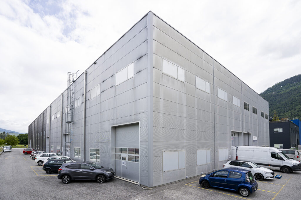 Light grey hall in Vétroz, seen from the opposite corner, with a roof ladder and a roller shutter