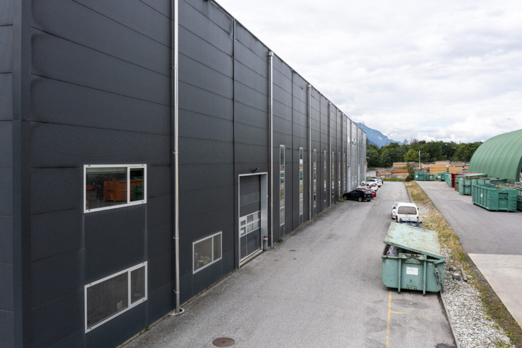 A view along the dark Valmont façade in Vétroz, showing the access road and skips