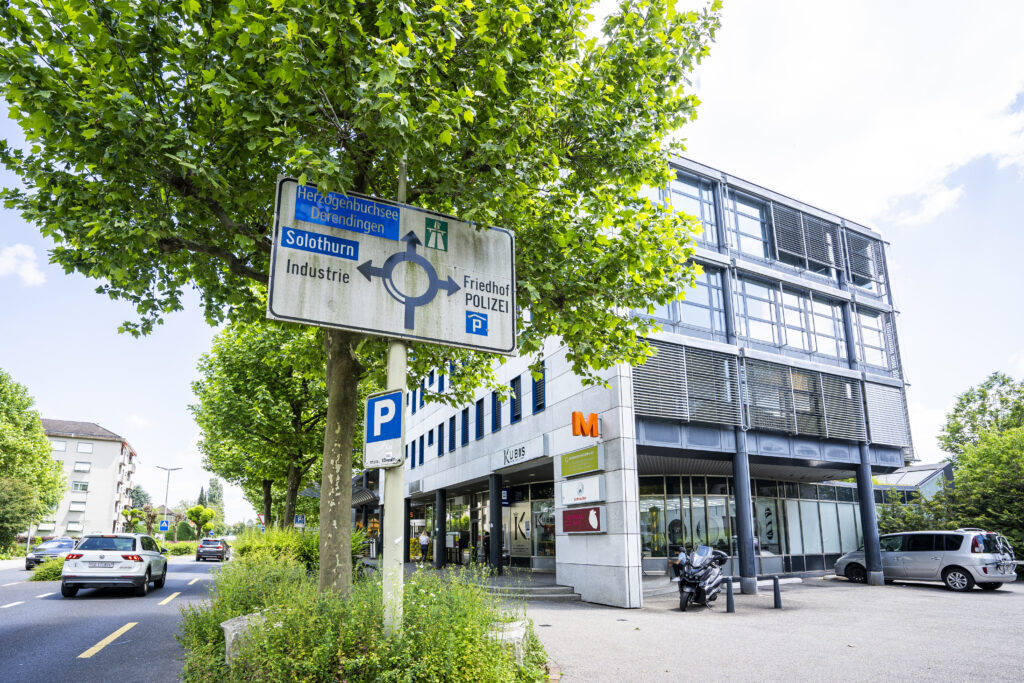 Commercial building in Zuchwil behind a signpost pointing towards Solothurn; the Migros ‘M’ is visible on the building