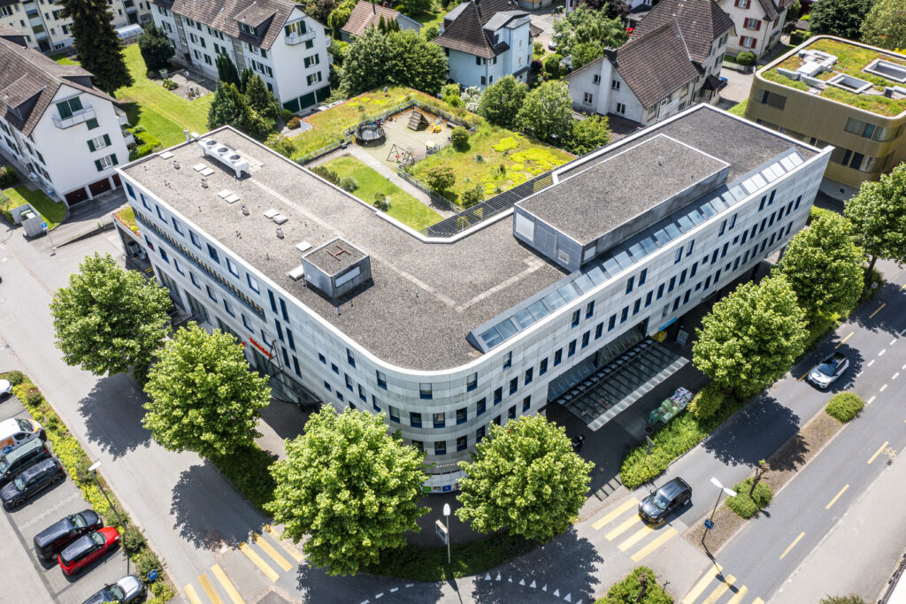 Aerial view of the curved Westgate commercial building in Zuchwil, with a roof garden and playground