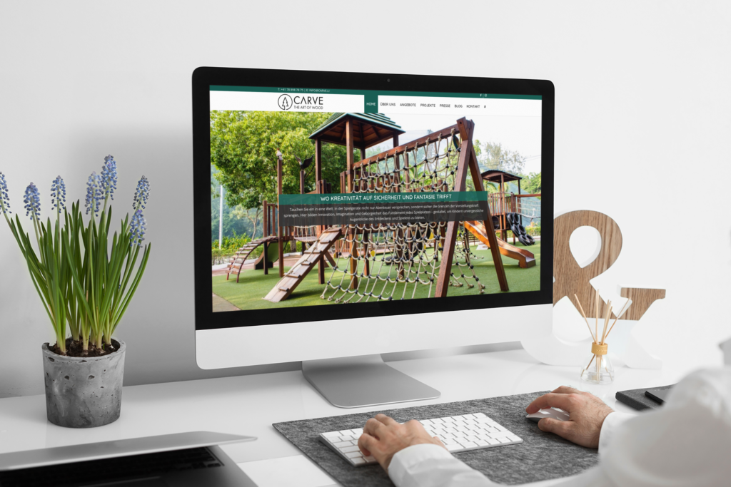 An iMac on a white desk with the Carve homepage and a wooden play tower