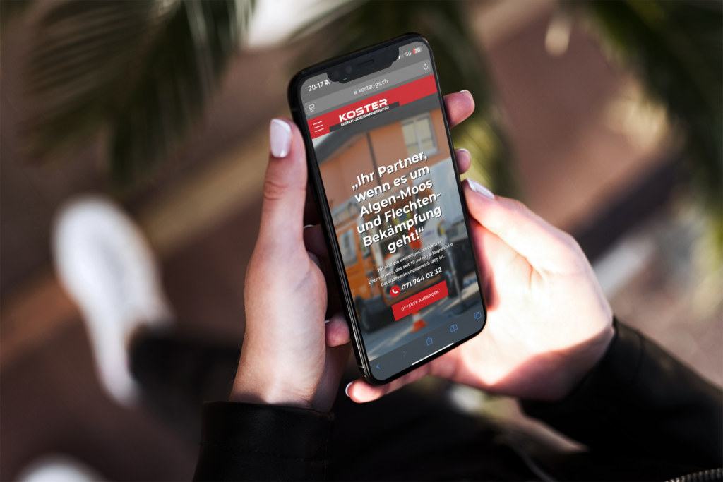 Hands holding an iPhone outdoors, viewing the Koster Gebäudesanierung mobile website