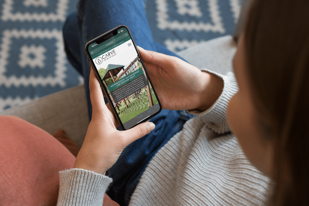 A woman on the sofa is holding an iPhone displaying Carve’s mobile website