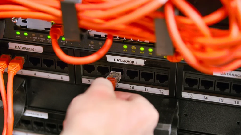 Hand steckt ein Netzwerkkabel in einen Serverschrank